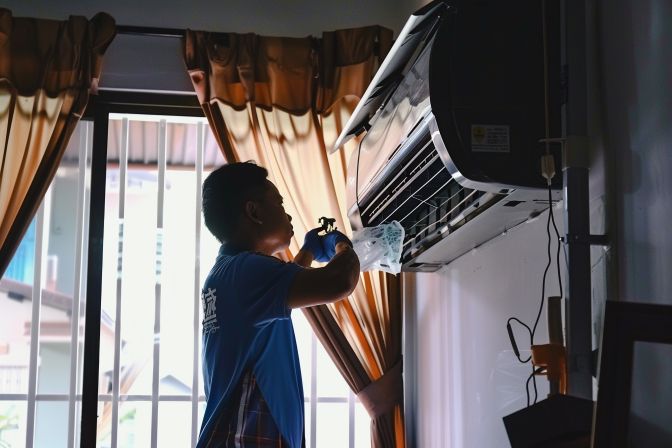 A technician performing air conditioning maintenance in a living room.