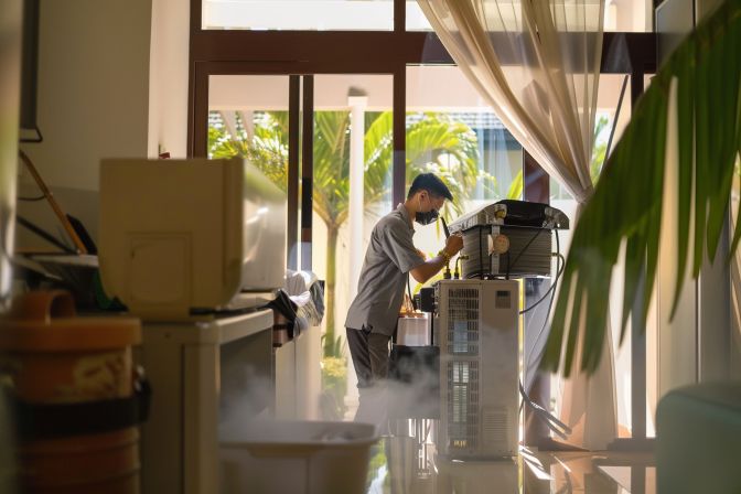 A technician in his 40s performing air conditioning servicing in a residential living room. A technician in his 40s performing air conditioning servicing in a residential living room.