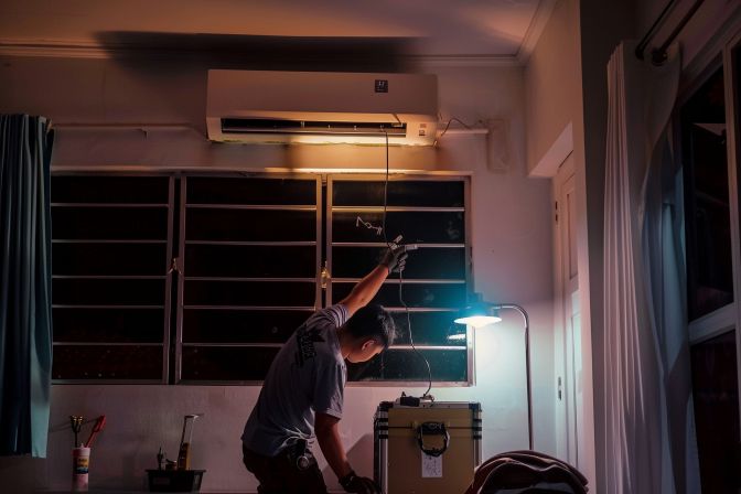 An air conditioning technician repairing a malfunctioning unit in a home. An air conditioning technician repairing a malfunctioning unit in a home.