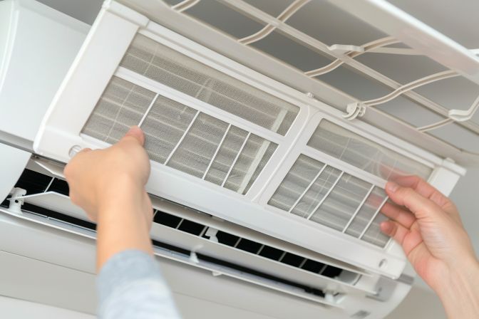 A close-up of hands removing an air filter from an HVAC unit. A close-up of hands removing an air filter from an HVAC unit.