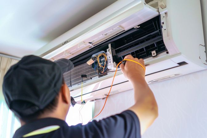 A technician is repairing a Mitsubishi aircon unit in a living room. A technician is repairing a Mitsubishi aircon unit in a living room.