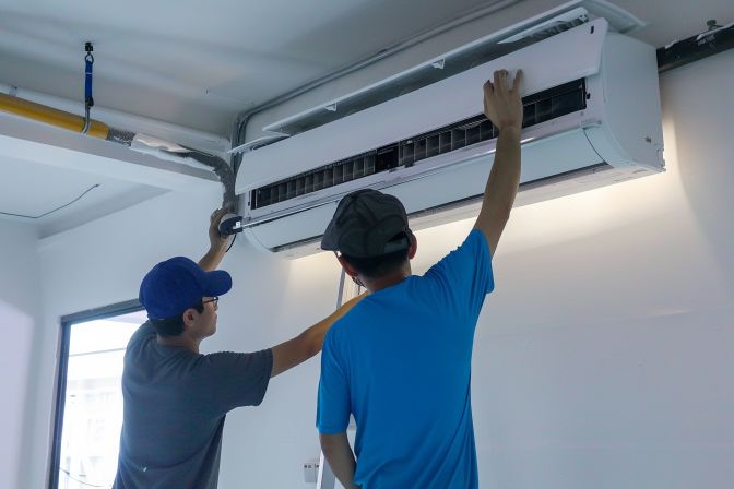 Two installers mounting a large air conditioning unit for efficient installation. Two installers mounting a large air conditioning unit for efficient installation.