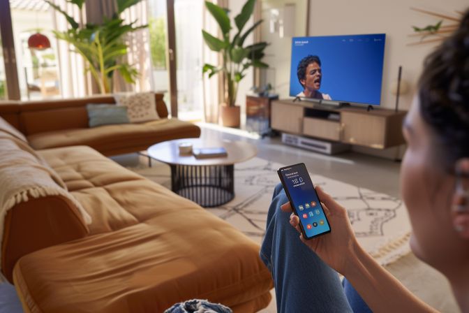 A person struggles to use an incompatible remote control with a modern smartphone. A person struggles to use an incompatible remote control with a modern smartphone.